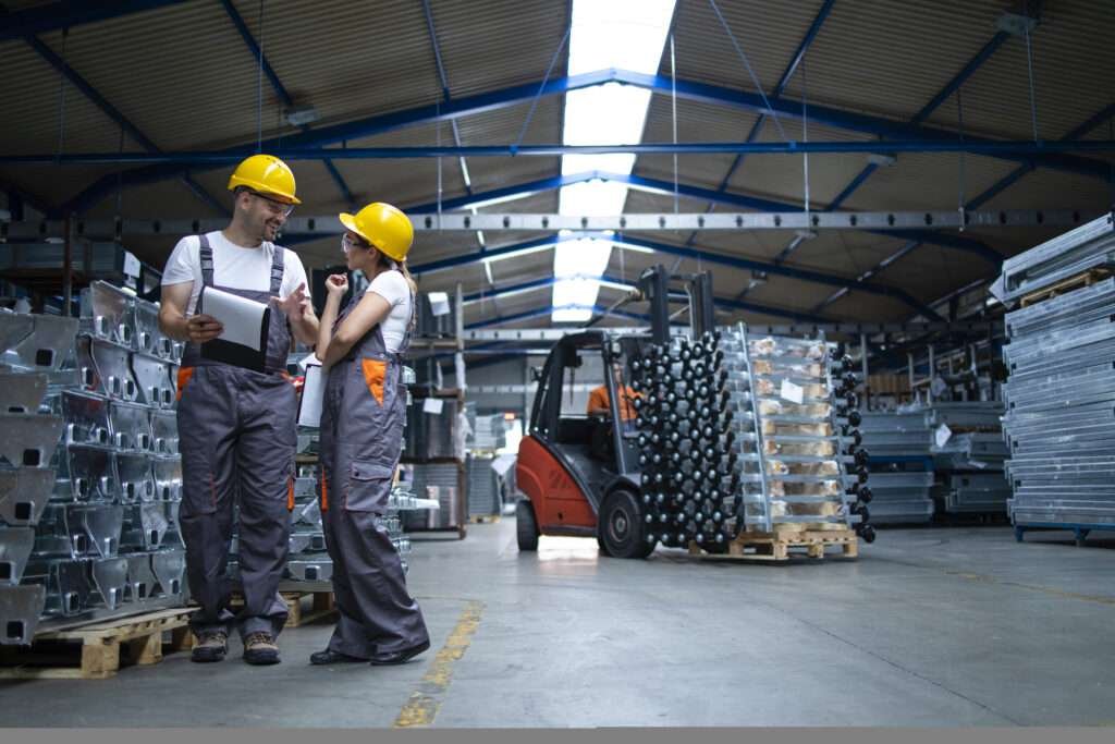 factory workers standing in industrial warehouse and discussing about production.